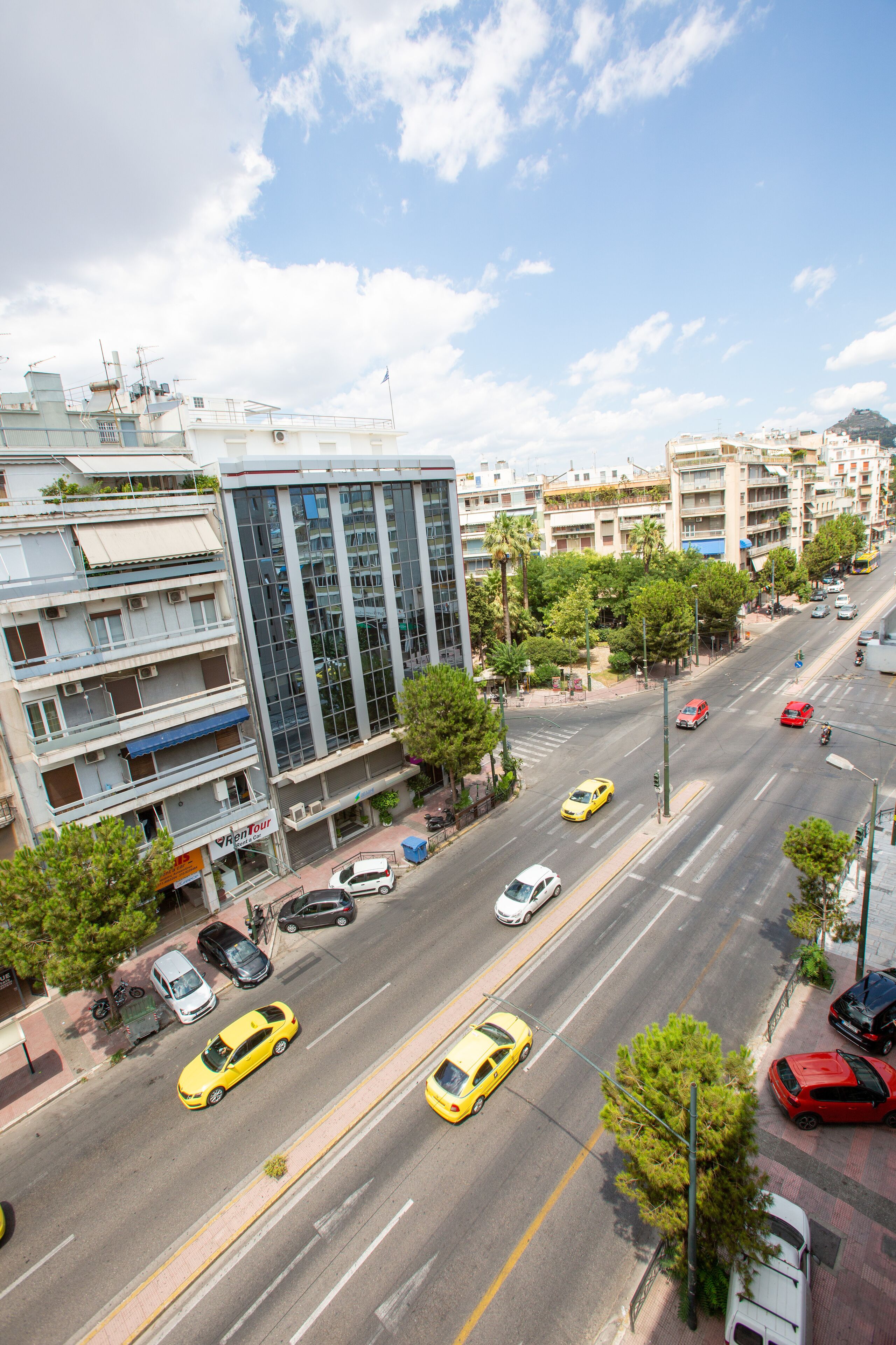 A multi-story building with a modern glass facade, located on a busy urban street with cars and taxis.