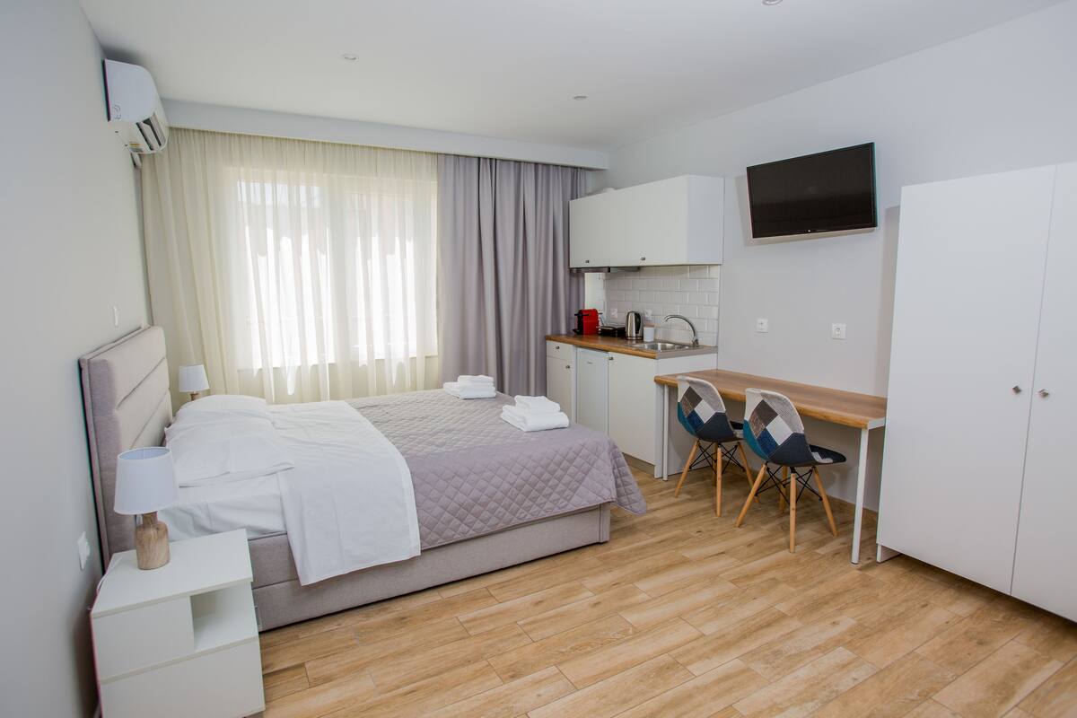 Habitación de hotel con cama, mesita de noche, escritorio, sillas, televisor y kitchenette.
