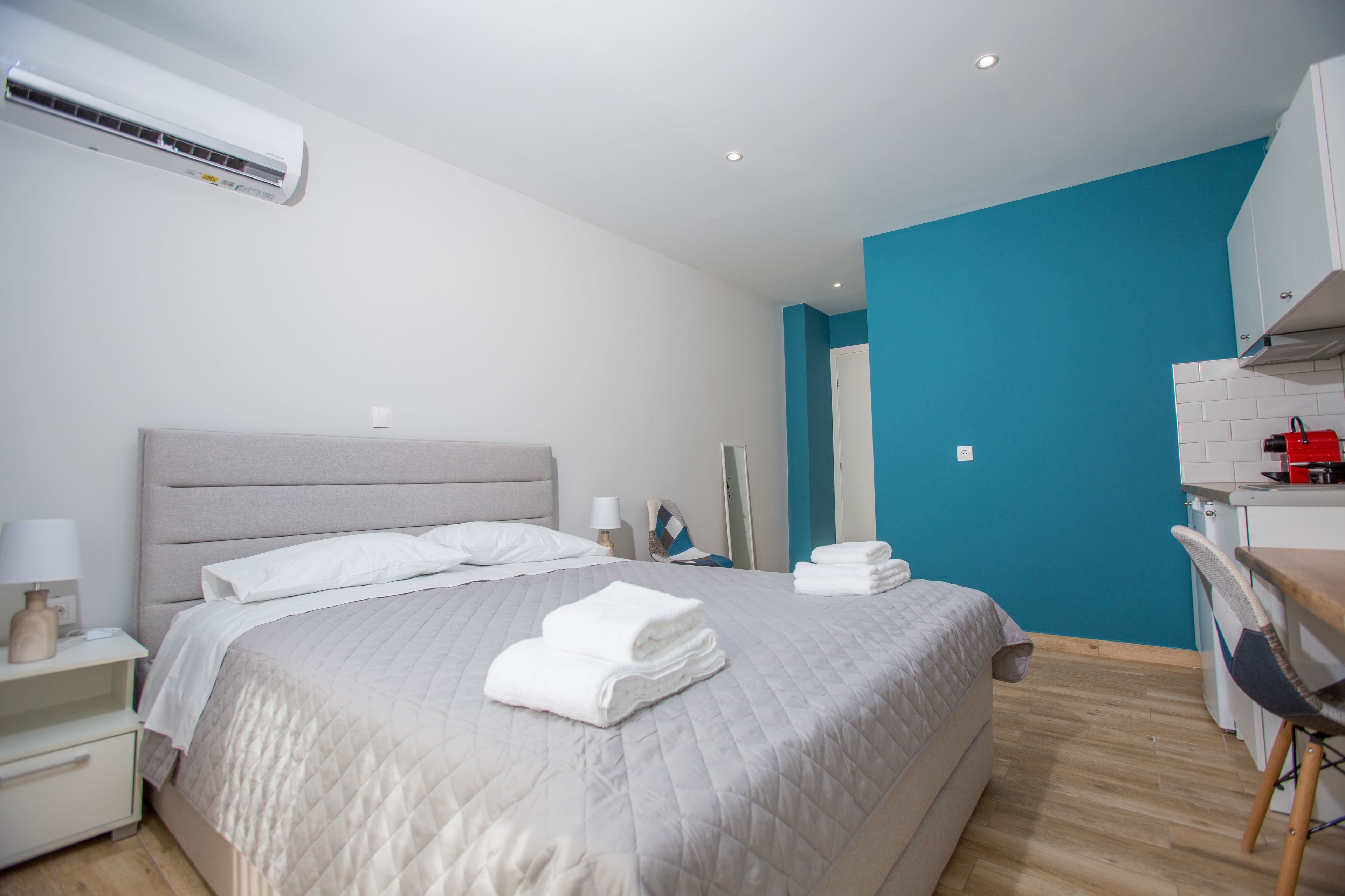 A modern hotel room with a large bed, a desk, and a kitchenette.