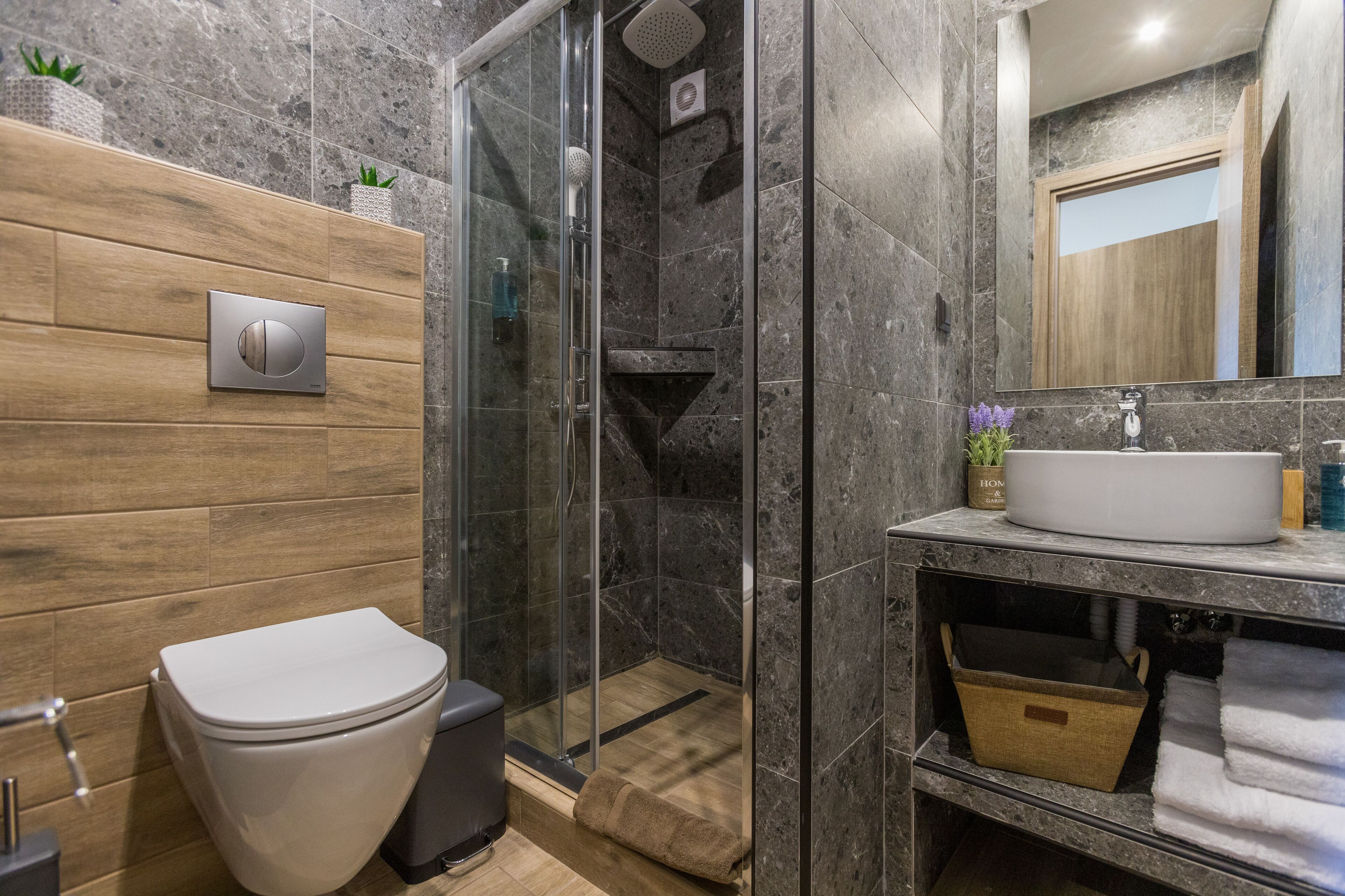 A modern bathroom with a glass-enclosed shower, a wooden vanity with a sink, and a toilet.