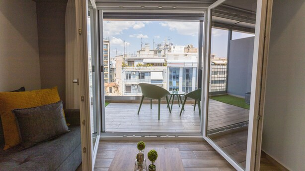 Una sala moderna con un sofá, una mesa de centro con objetos decorativos, y vista a un balcón exterior con sillas y una mesa.
