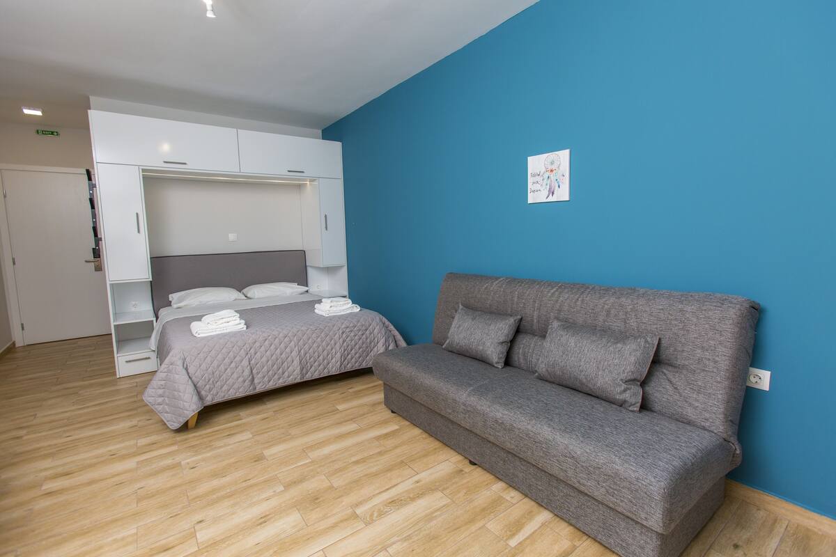 Un dormitorio con una cama, un sofá gris, un armario y una pared azul.