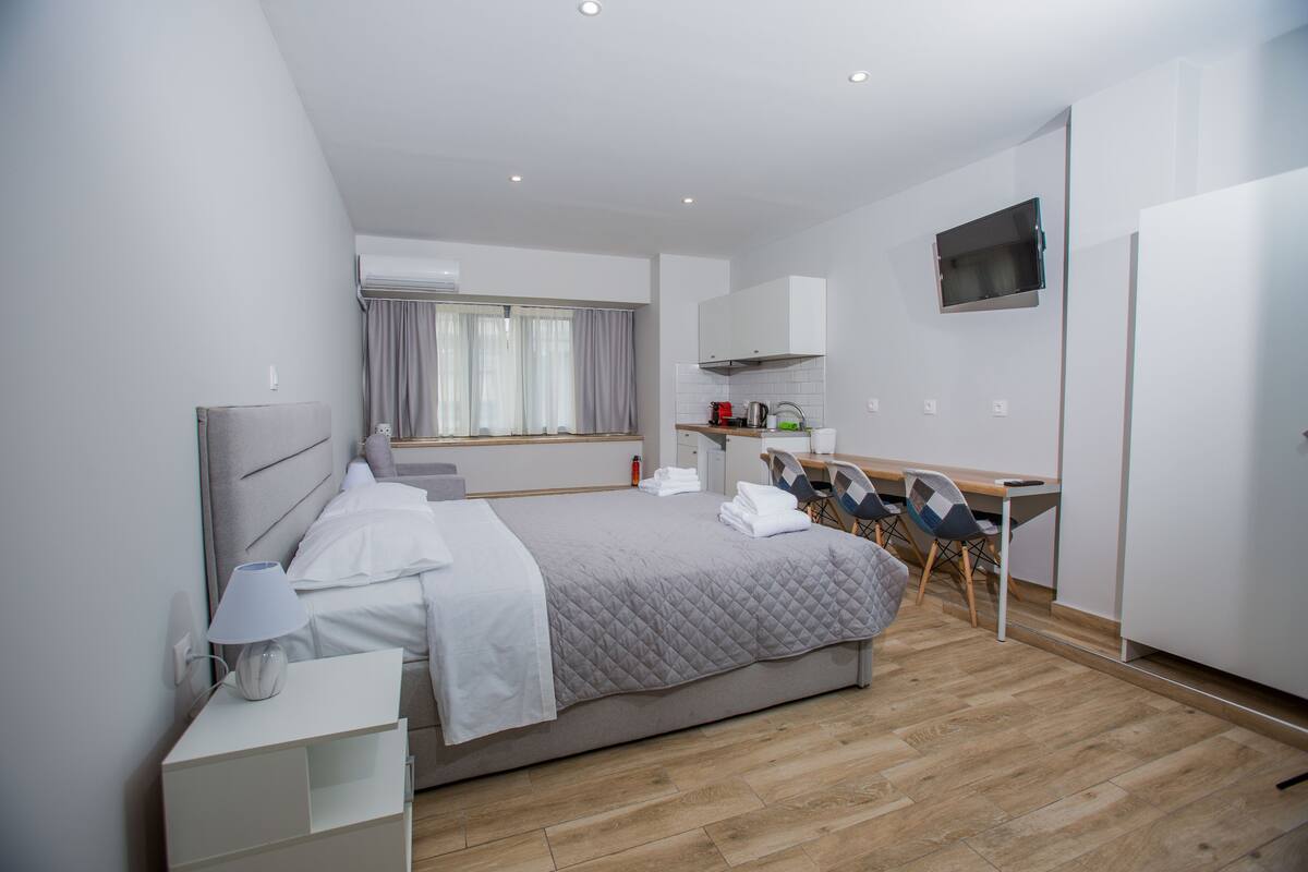 Una habitación de hotel moderna con una cama grande, un escritorio con sillas, un televisor y una kitchenette.