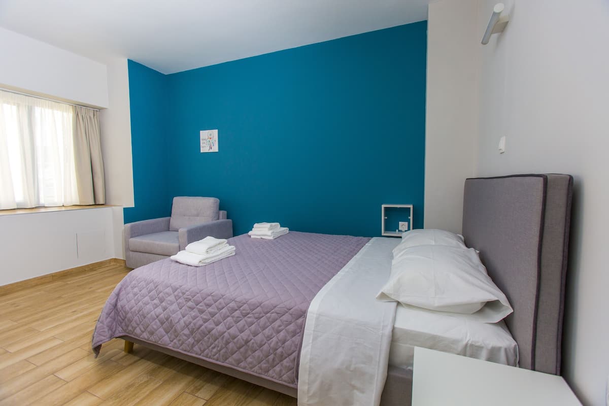 Una habitación de hotel moderna con una cama grande, un sillón gris y una mesita.