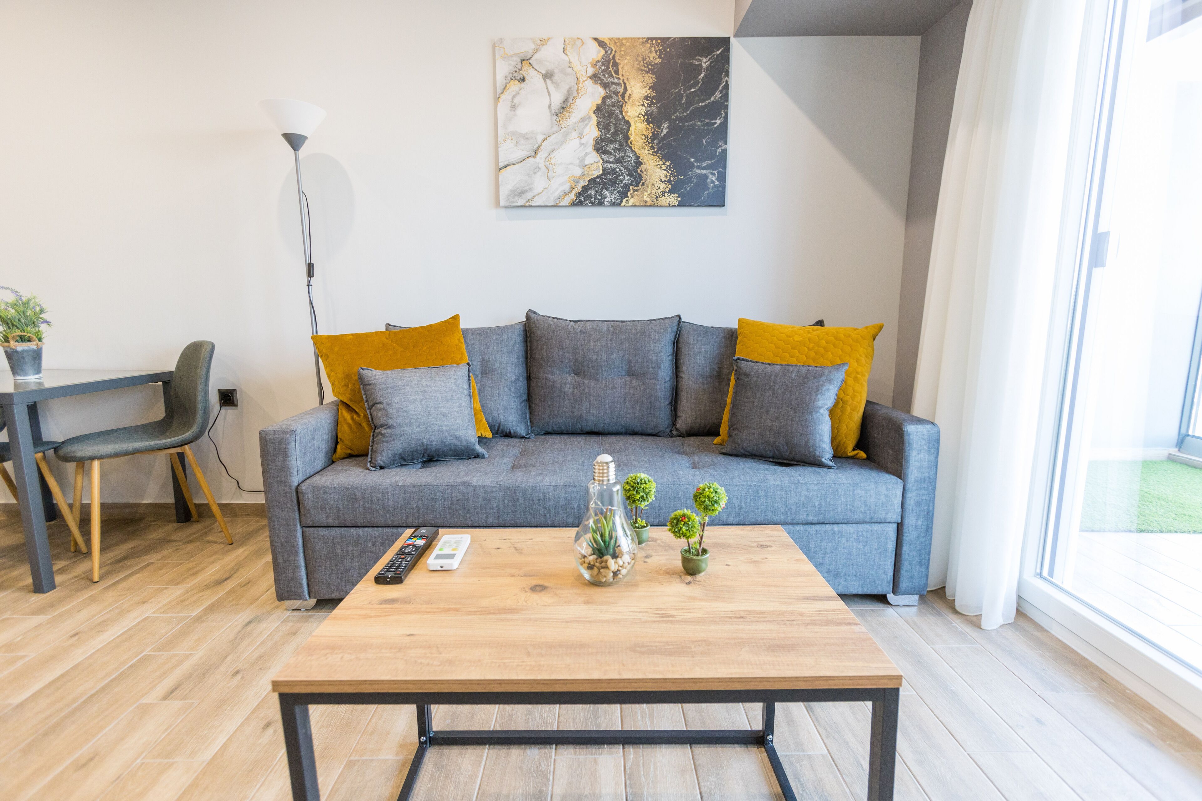 A modern living room with a grey sofa, yellow cushions, a wooden coffee table, and a marble artwork on the wall.