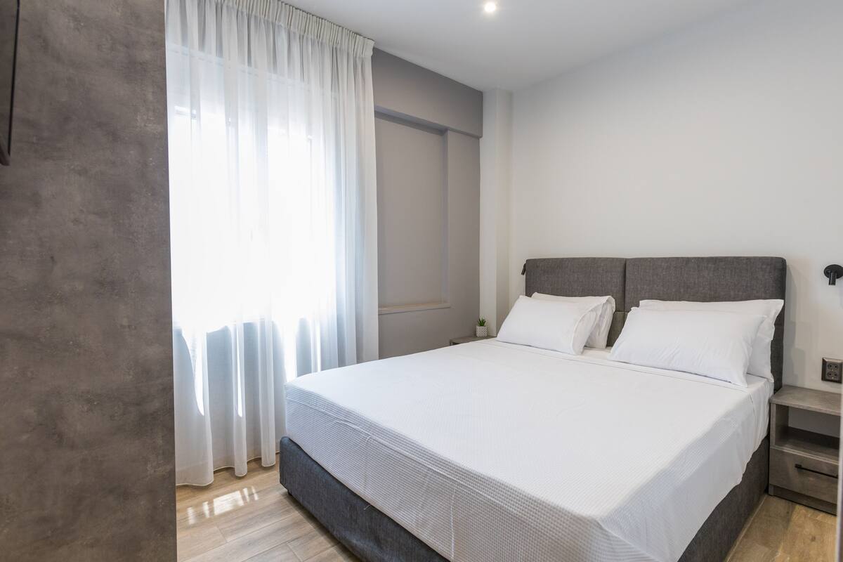 Un dormitorio moderno con una cama grande, una mesita de noche y una ventana con cortinas translúcidas.