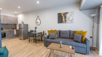 A modern living room with a grey sofa, wooden coffee table, and a dining area with a small table and chairs.