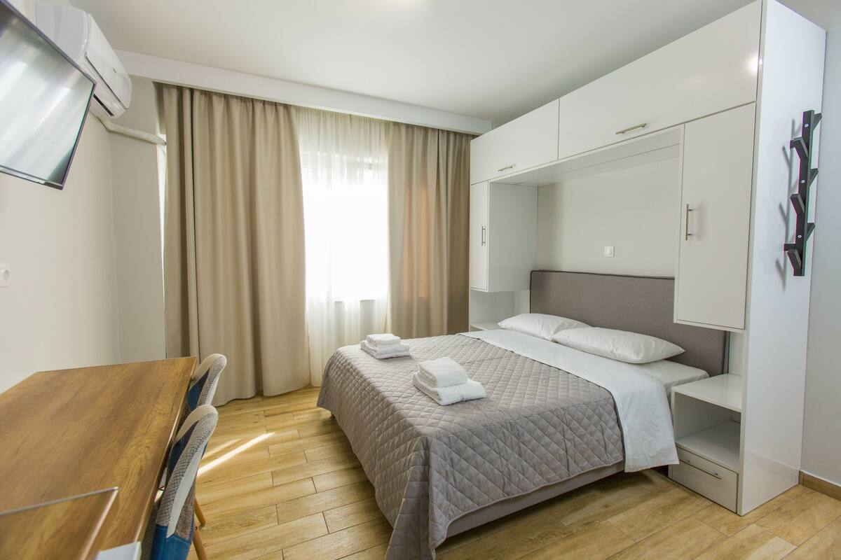 Una habitación de hotel con una cama, un escritorio de madera, un armario y un televisor fijado en la pared.
