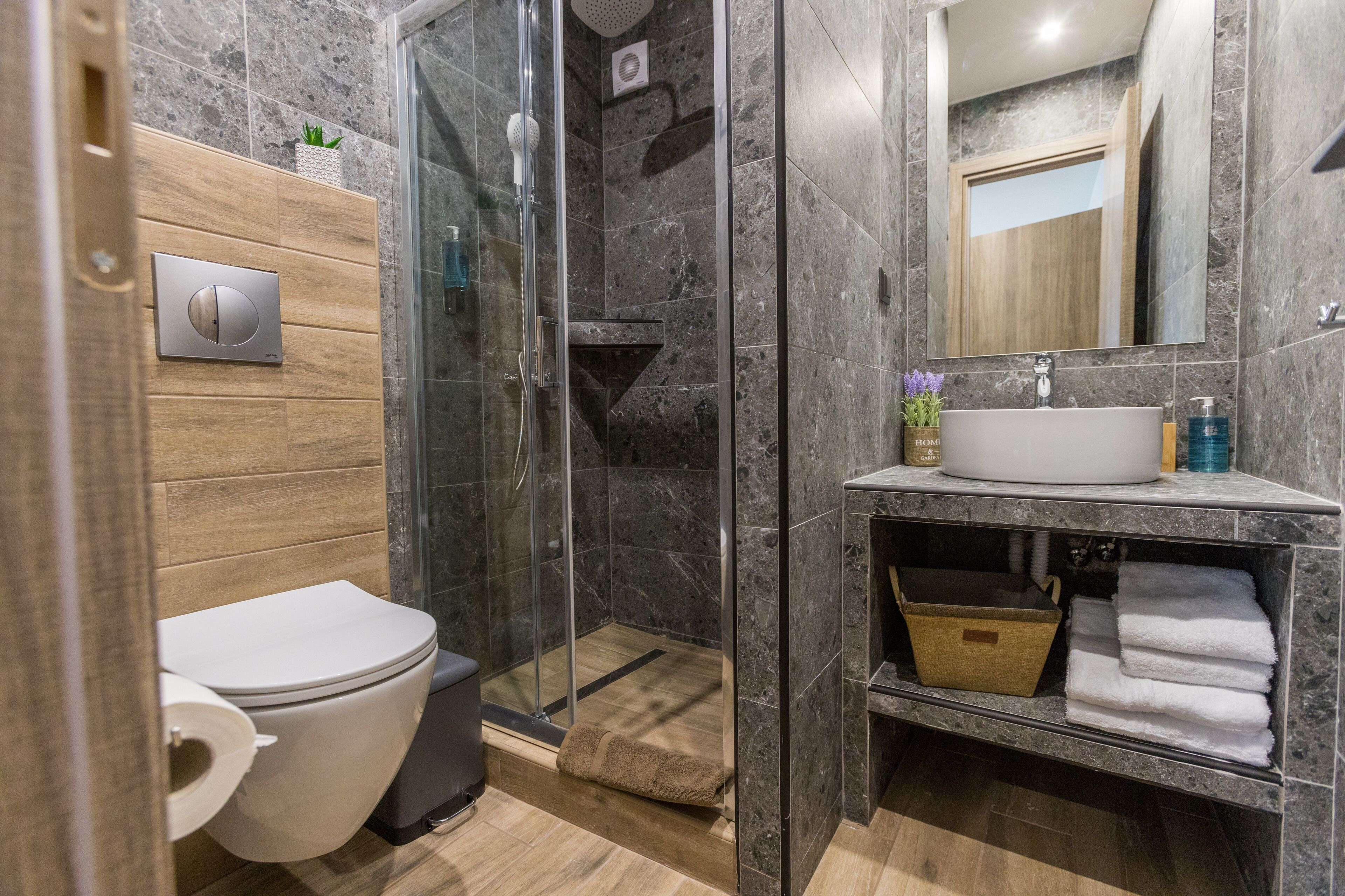 A modern bathroom with a glass-enclosed shower, a toilet, a sink with a mirror, and a wooden vanity.