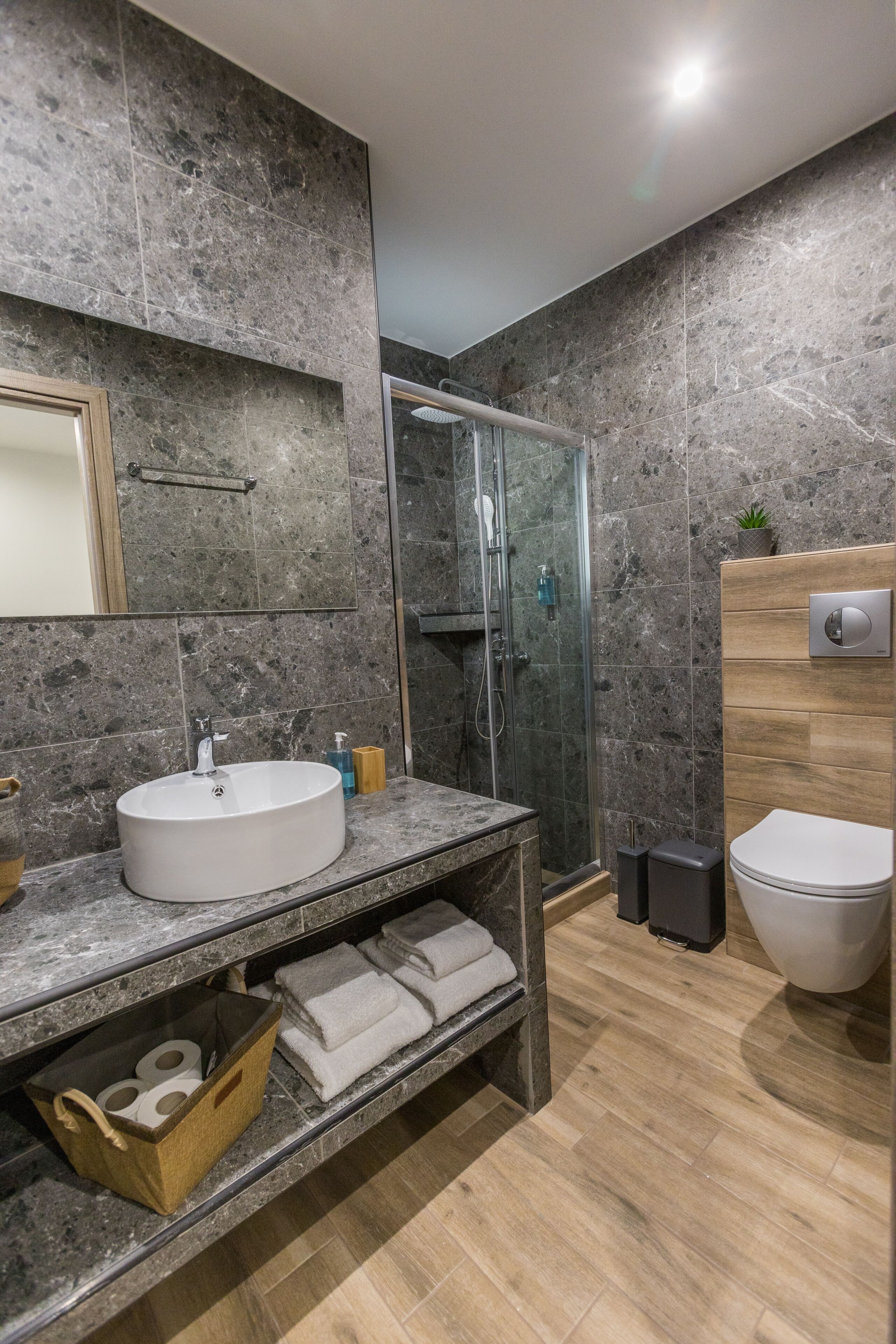 Une salle de bain moderne avec un lavabo en marbre, un meuble-lavabo en bois et une cabine de douche en verre.