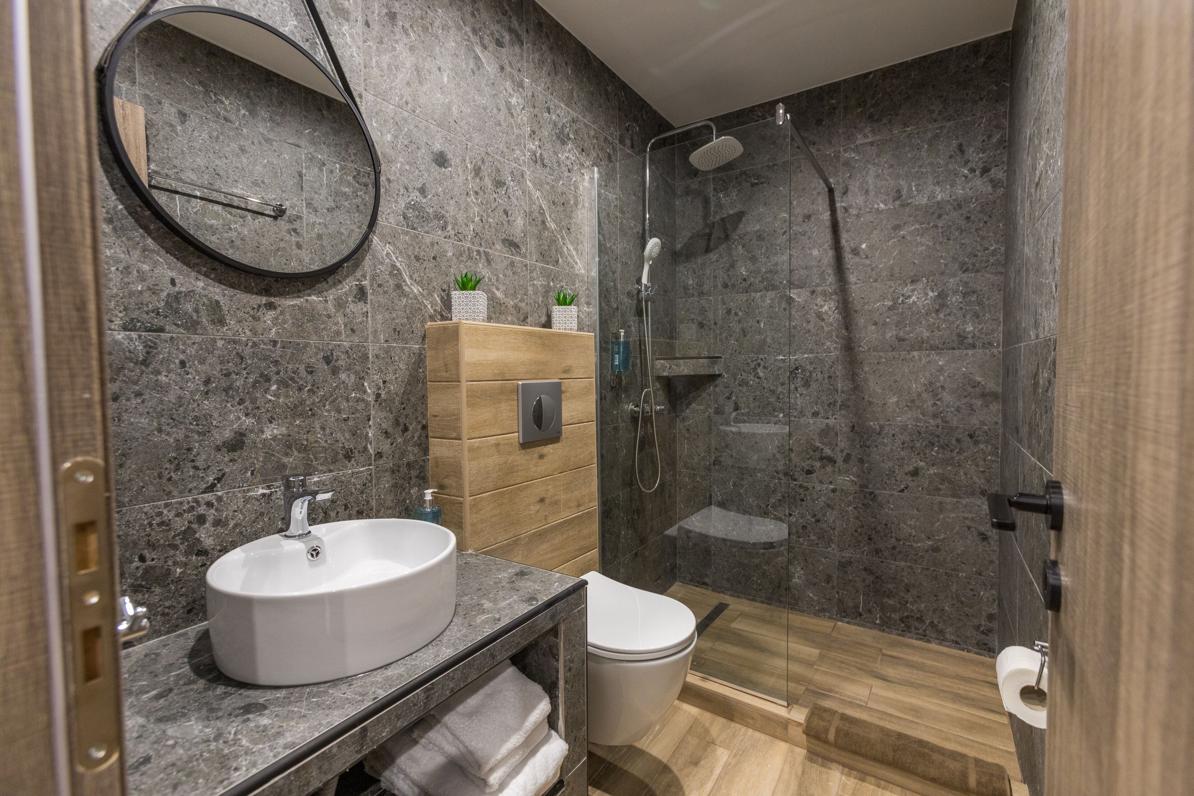 A modern bathroom with a marble sink, wooden vanity, and a glass-enclosed shower.