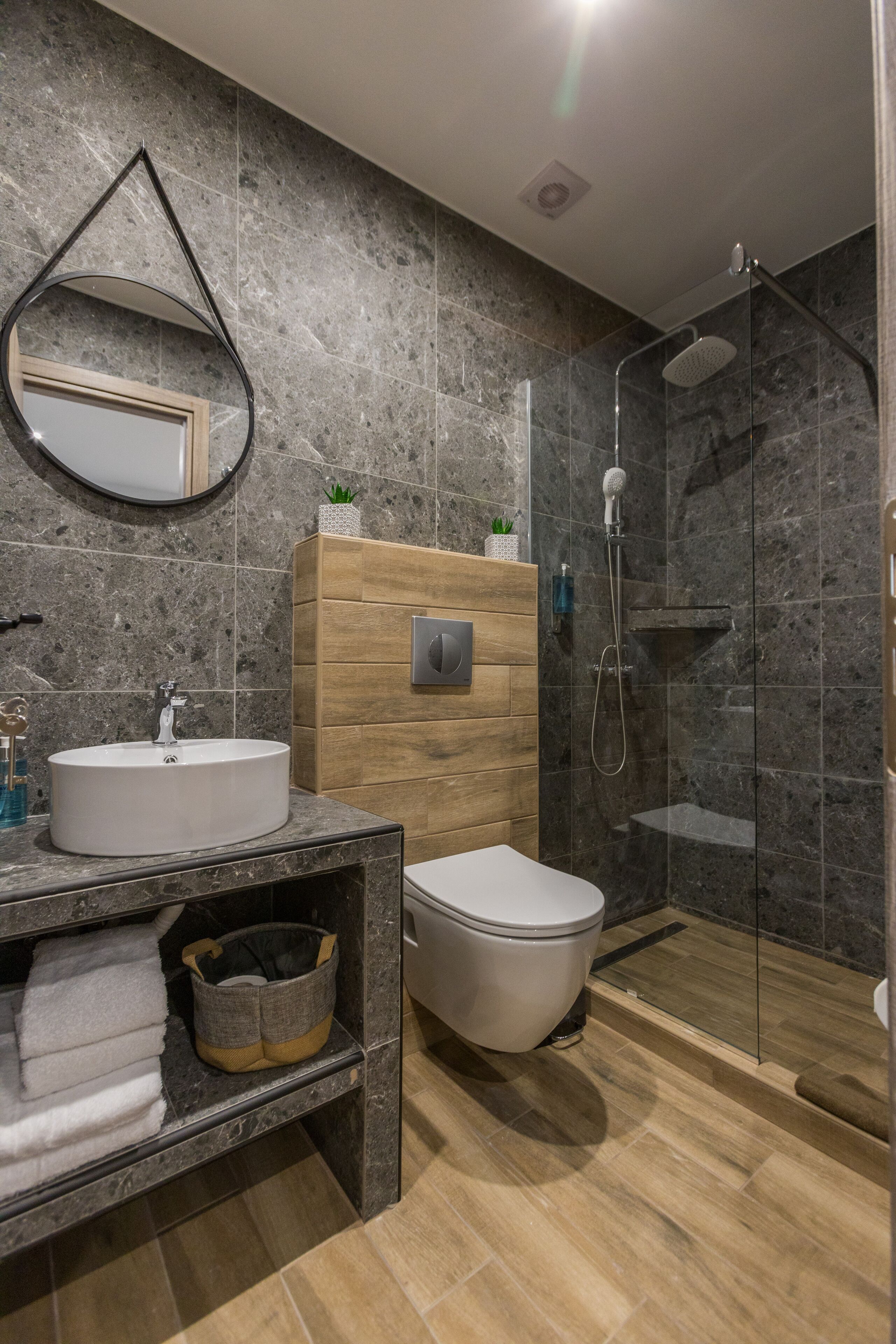 A modern bathroom with a marble sink, wooden vanity, a toilet, and a glass-enclosed shower.