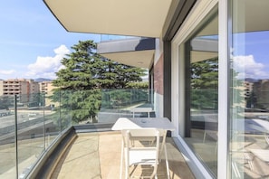 A balcony with a glass railing, a white table, and a chair. - Roggia Apartments (Lugano)