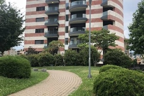 A multi-story residential building with balconies, surrounded by greenery and a paved pathway. - Roggia Apartments (Lugano)