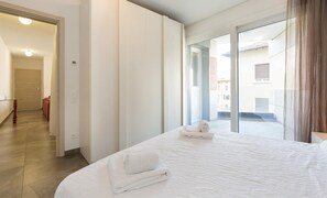 A hotel room with a large bed, a glass door leading to a balcony, and a view of the outside. - Roggia Apartments (Lugano)