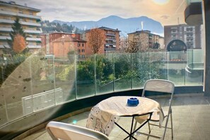 A balcony with a table and chairs, a glass railing, and a view of buildings and mountains in the background. - Roggia Apartments (Lugano)