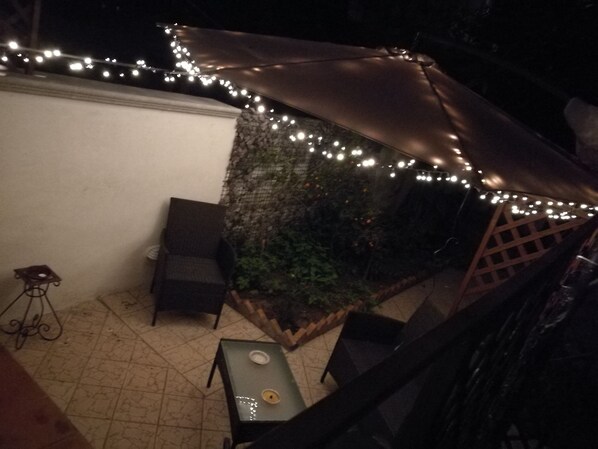 A patio area with a table and chairs, a small table with a bowl, and a string of lights. - Bella Palermo (Palermo)