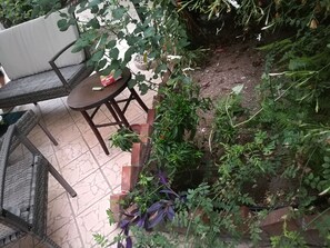 Eine Terrasse mit rundem Tisch und Stühlen, umgeben von Blumentöpfen und einer kleinen Gartenanlage.