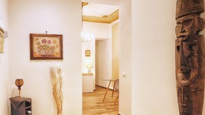 A hallway with a wooden floor, a framed floral painting, a tall vase with branches, and a wooden sculpture. - Bella Palermo (Palermo)