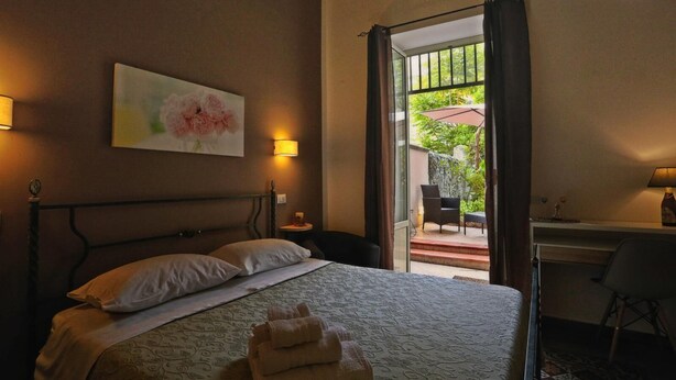 A hotel room with a bed, a desk, and a view of an outdoor area with a patio and chairs. - Bella Palermo (Palermo)