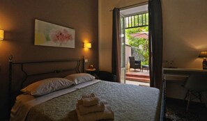 A hotel room with a bed, a desk, and a view of an outdoor area with a patio and chairs. - Bella Palermo (Palermo)