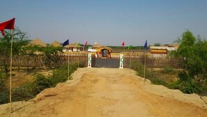Un chemin de terre mène à un bâtiment doté d’une porte, entouré de huttes aux toits de chaume et de drapeaux.