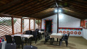 Un espace de restauration abrité, avec des tables et des chaises, un mur blanc orné de motifs colorés et un plafond en bois.