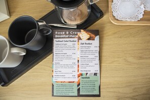 A breakfast menu on a wooden table with a coffee pot, a black mug, and a white teapot. - Rose and Crown (Poole)