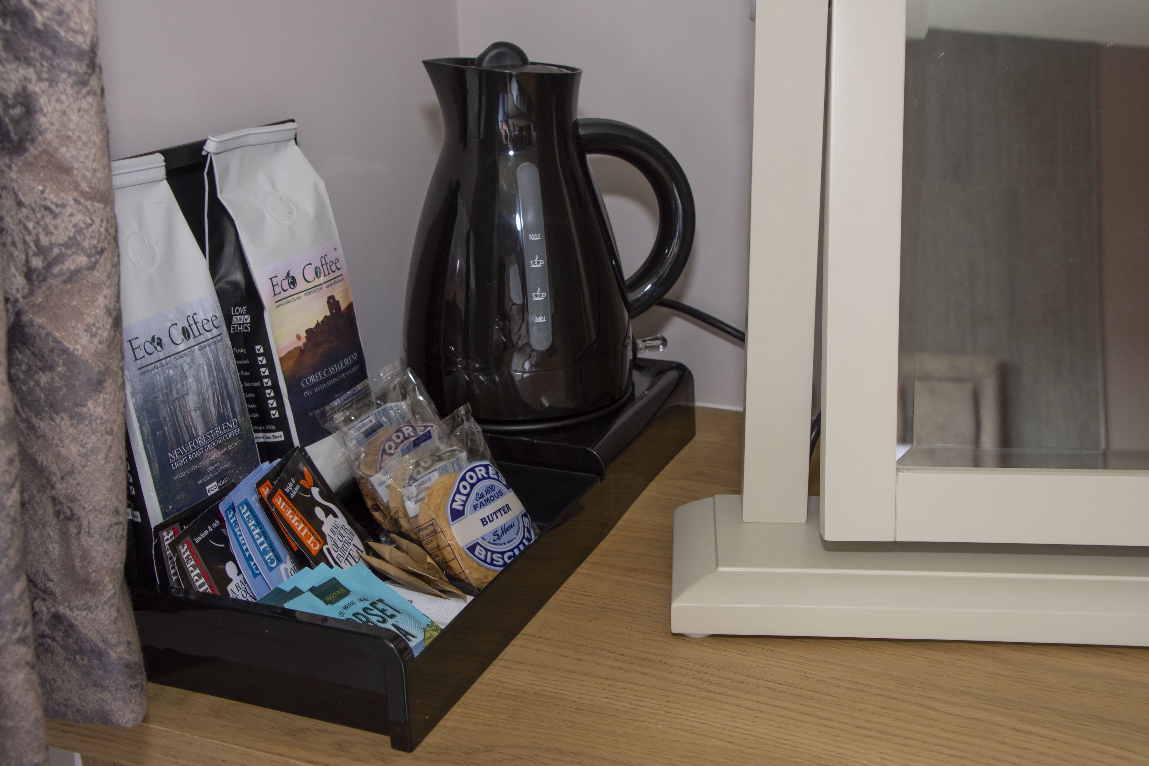 A coffee station with a coffee maker, bags of coffee, and a tray of snacks.