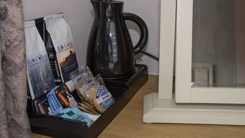 A coffee station with a coffee maker, bags of coffee, and a tray of snacks.
