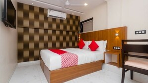 A hotel room with a bed, a wooden headboard, a TV, an air conditioning unit, and a ceiling fan. - Hotel Qubestay Airport (Mumbai)
