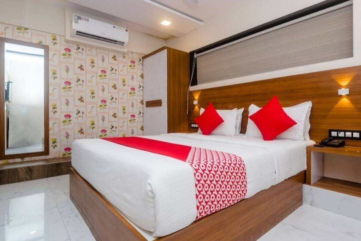 A hotel room with a large bed, a bedside table with a phone, and a wall-mounted air conditioner.