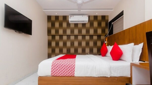 A hotel room with a bed, a flat-screen TV mounted on the wall, an air conditioning unit, and a wooden headboard. - Hotel Qubestay Airport (Mumbai)