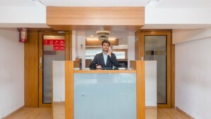 A reception area with a wooden reception desk, a fire extinguisher, and a glass door. - Hotel Qubestay Airport (Mumbai)