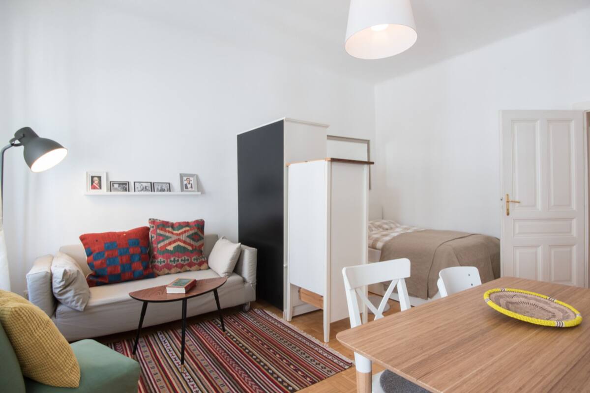 Un espacio habitable moderno y funcional con sofá, una pequeña mesa, una mesa de comedor, una lámpara y una cama.