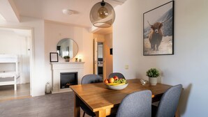 Un coin repas avec une table en bois, des chaises grises, un saladier de fruits et une cheminée.