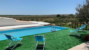 A pool with artificial grass, two lounge chairs, a wooden fence, and a potted plant.