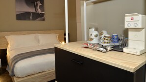 A hotel room with a bed, a desk with a coffee maker, cups, and a small cabinet.