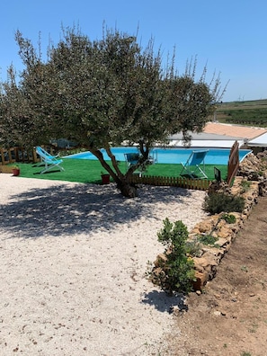 Un espace piscine avec une plage de sable, un arbre et un ciel bleu dégagé.