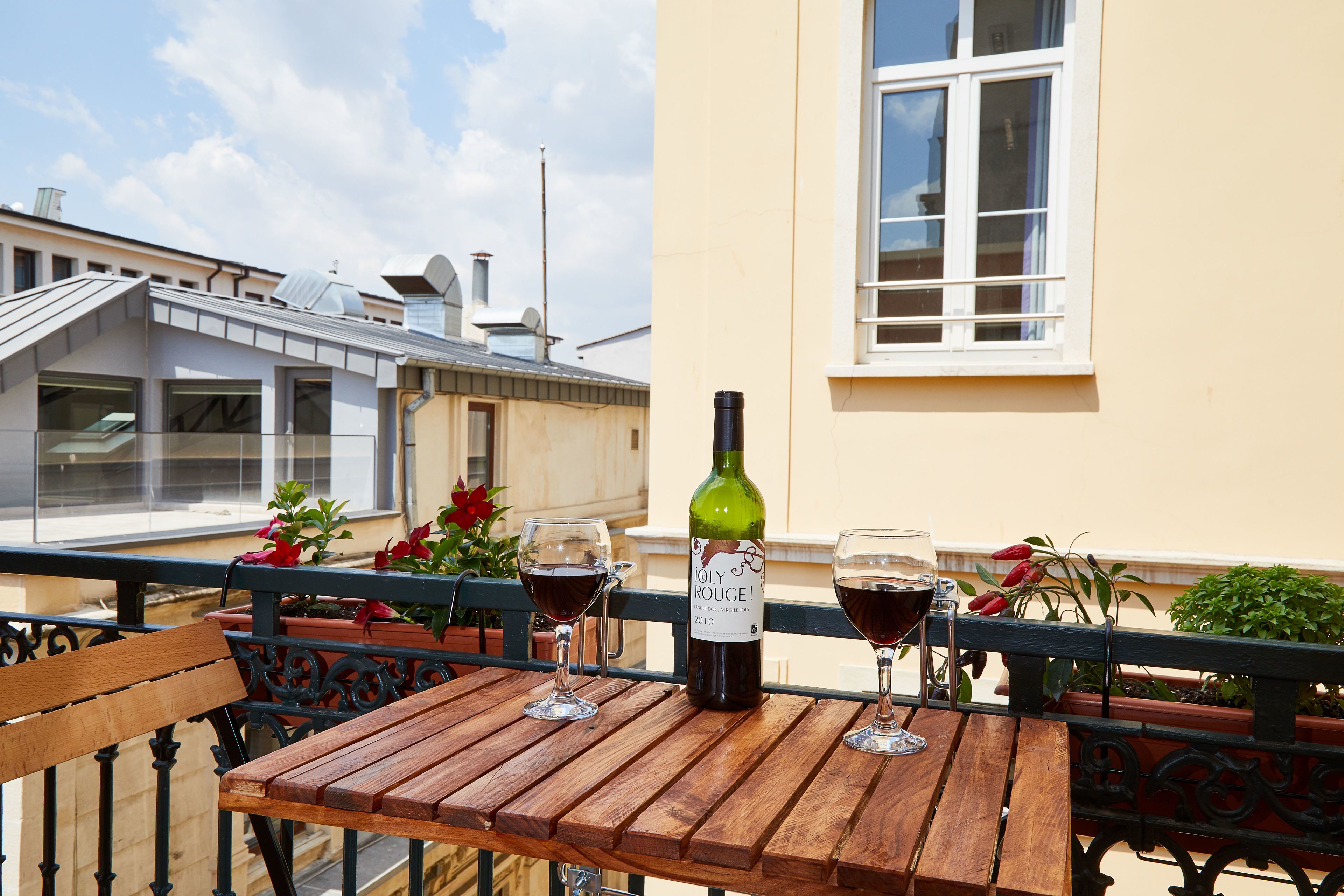 Une table en bois avec une bouteille de vin et deux verres, sur un balcon.