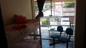 A room with a bunk bed, a small table with chairs, and a view of the street outside. - Pousada Casa da Regina (Guarujá)