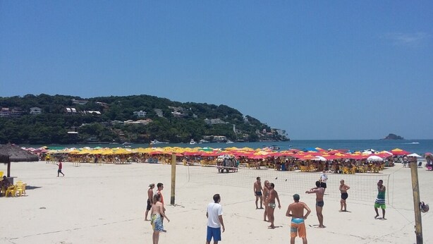 A beach volleyball court with people playing, surrounded by colorful umbrellas and beach chairs. - Pousada Casa da Regina (Guarujá)