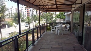A covered balcony with a table and chairs, overlooking a street with palm trees and buildings. - Pousada Casa da Regina (Guarujá)