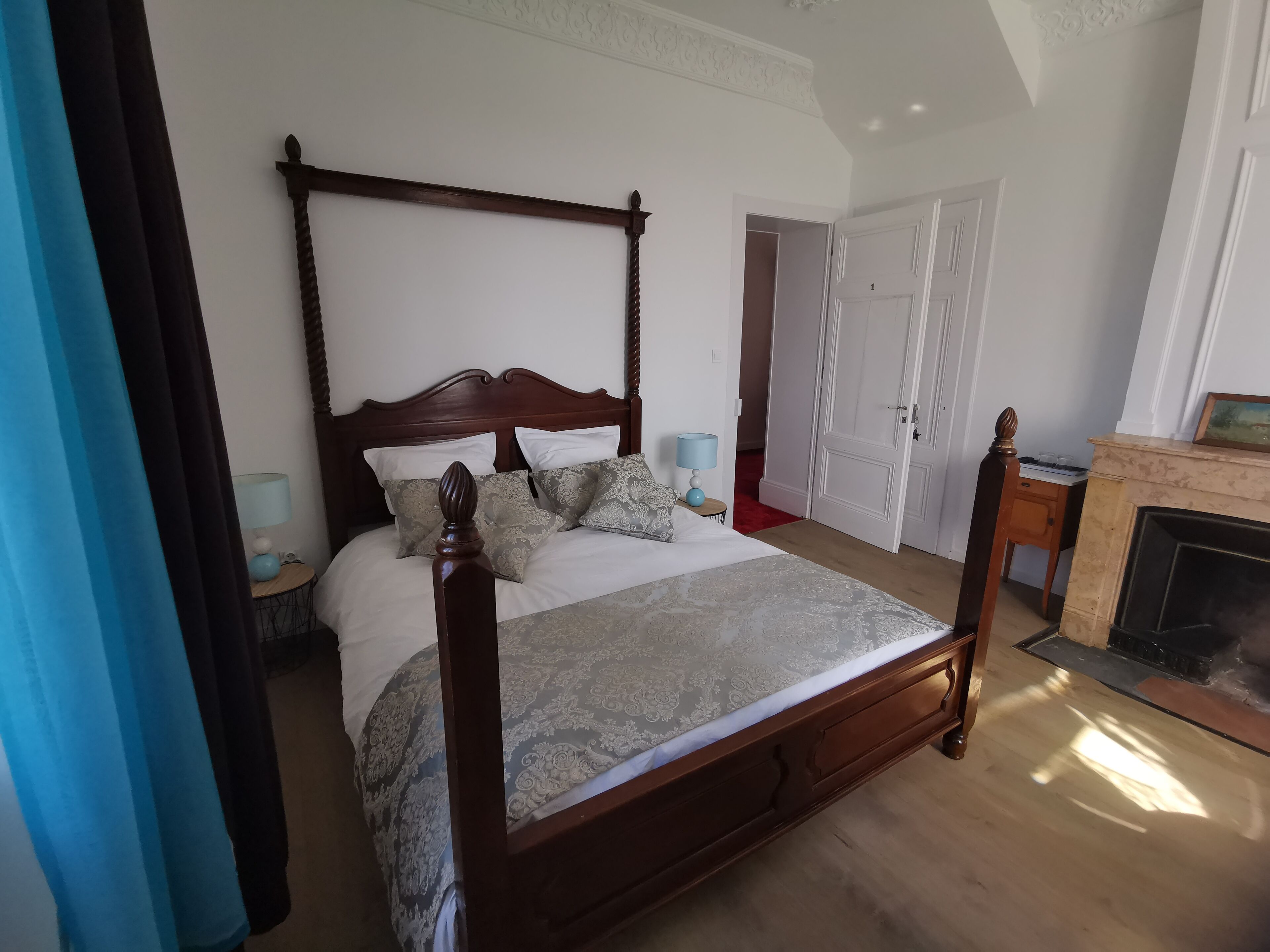 A four-poster bed with a wooden headboard, a bedside table with a lamp, and a fireplace.