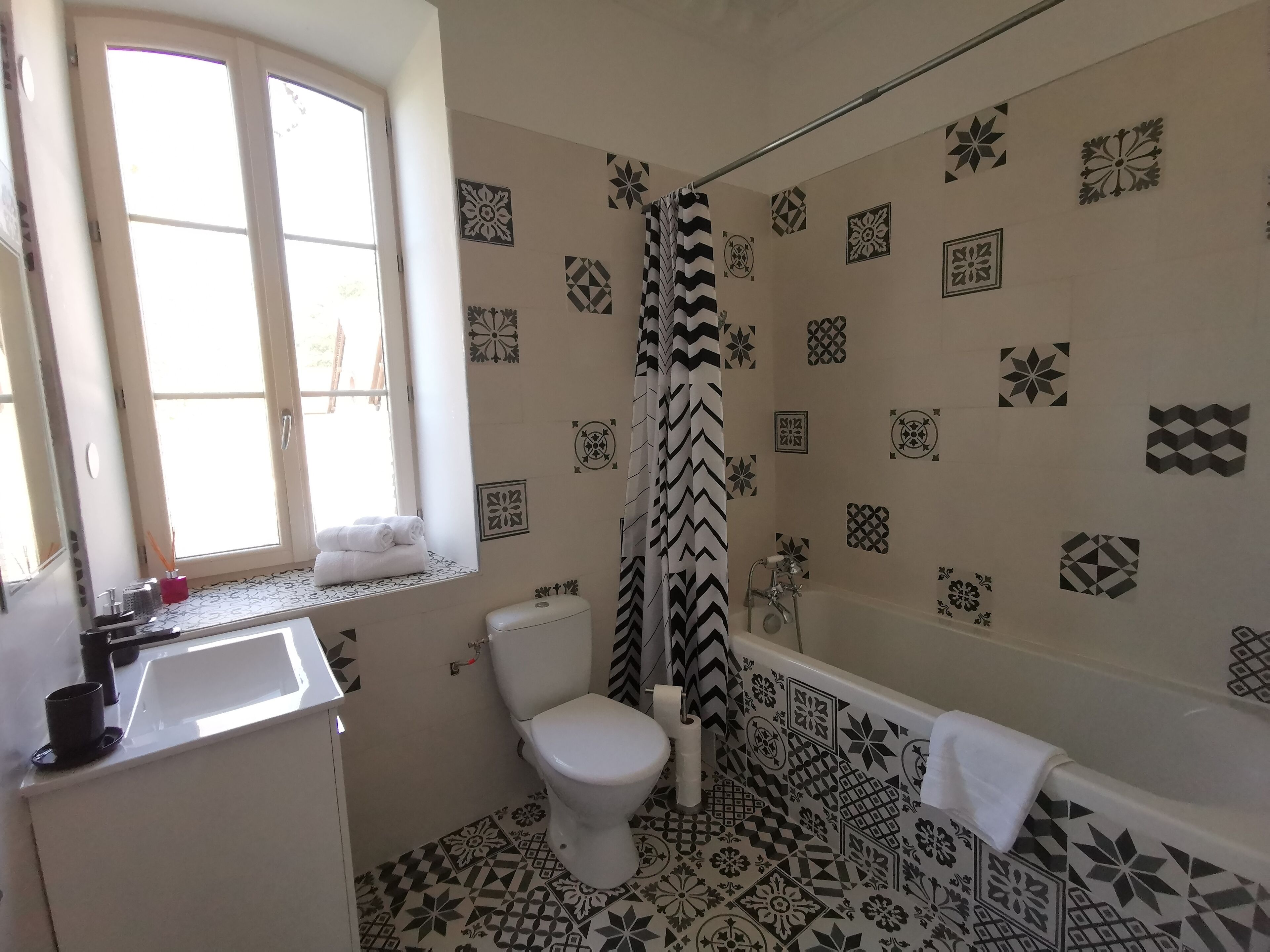 Un baño con inodoro, lavamanos y bañera. Las paredes presentan diseños geométricos y florales.
