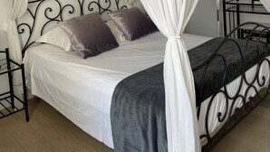 Una cama con dosel y cuatro columnas, con ropa de cama blanca y un edredón gris.