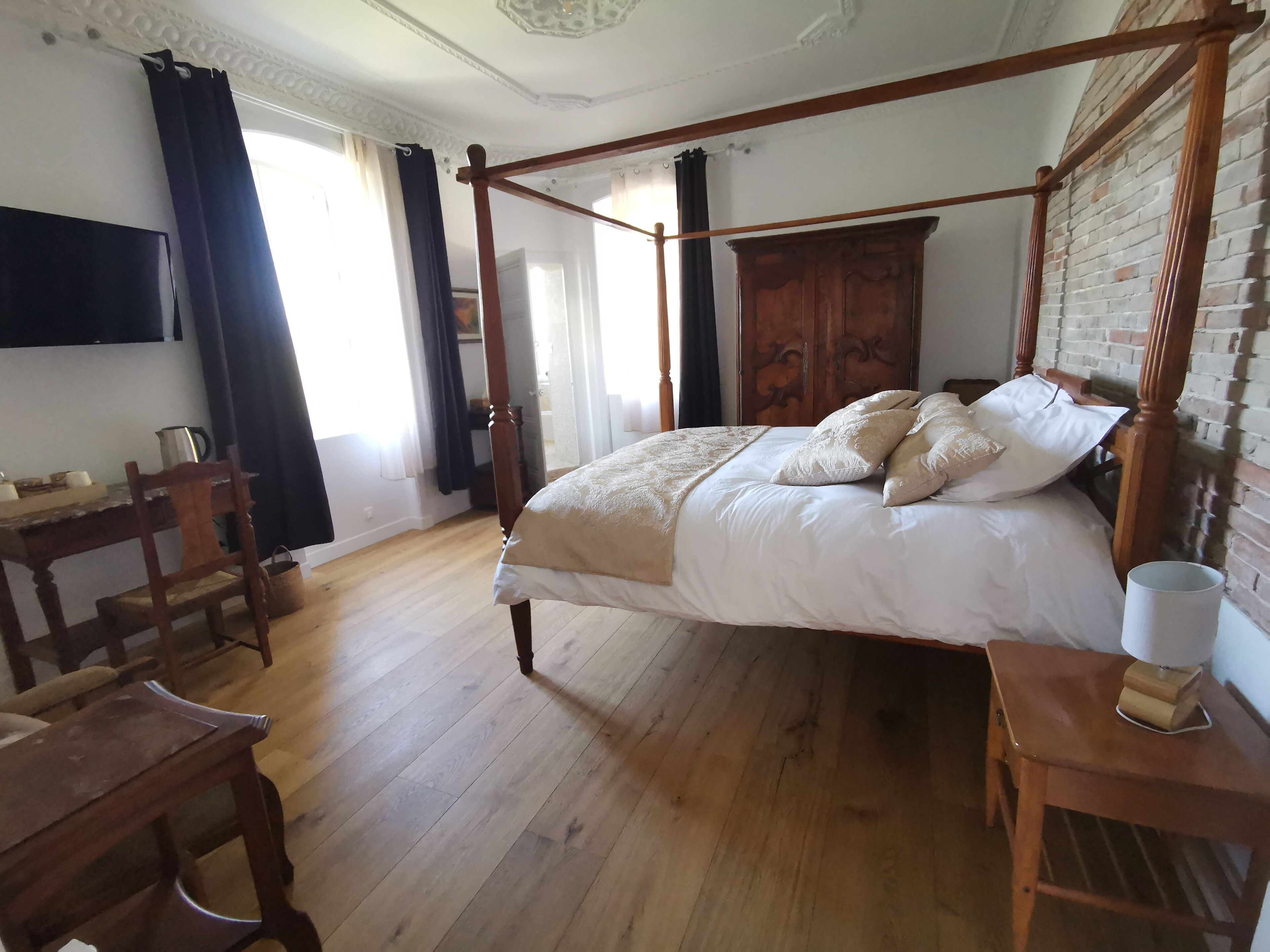 A four-poster bed with a wooden headboard, a bedside table with a lamp, and a wooden chair.