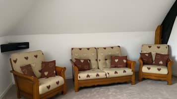 Une chambre à coucher de style loft avec un plafond en pente, deux fauteuils en bois, un canapé et un téléviseur fixé au mur.