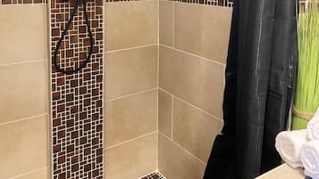 Un espace douche doté d’une pomme de douche à effet pluie, d’un rideau de douche noir et d’un mur carrelé orné d’un motif en mosaïque.