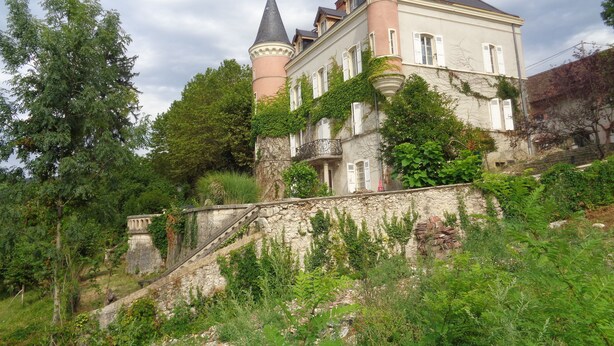 Un edificio histórico con una torre, rodeado de exuberante vegetación y una escalera de piedra.